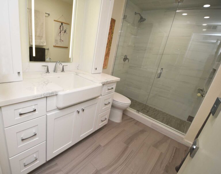 Bathroom vanity with an apron front sink and a stone top, beside a glass shower.
