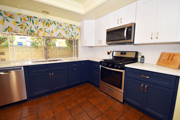 The same kitchen after remodelling, with navy blue base cabinets, white upper cabinets and new counters, on the original tile floor.