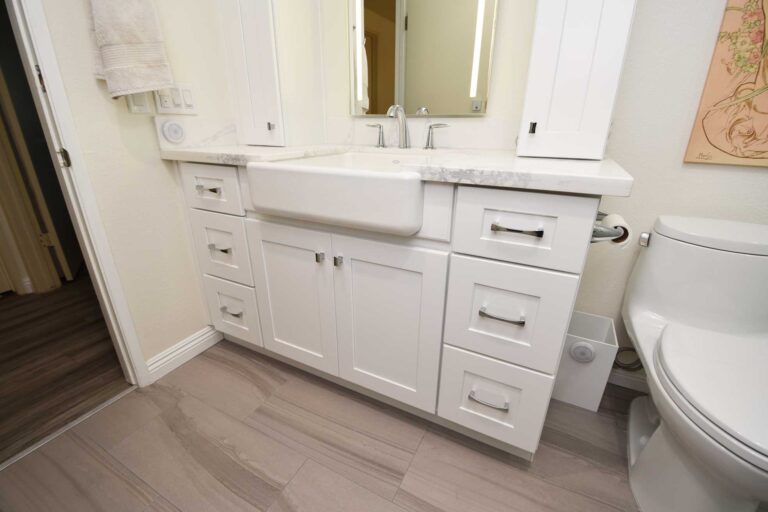 White bathroom vanity with an apron front sink, drawers and a stone top.