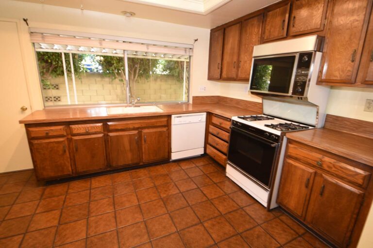 Kitchen before remodelling, with dated oak cabinets, a laminate counter and a terracotta tile floor.
