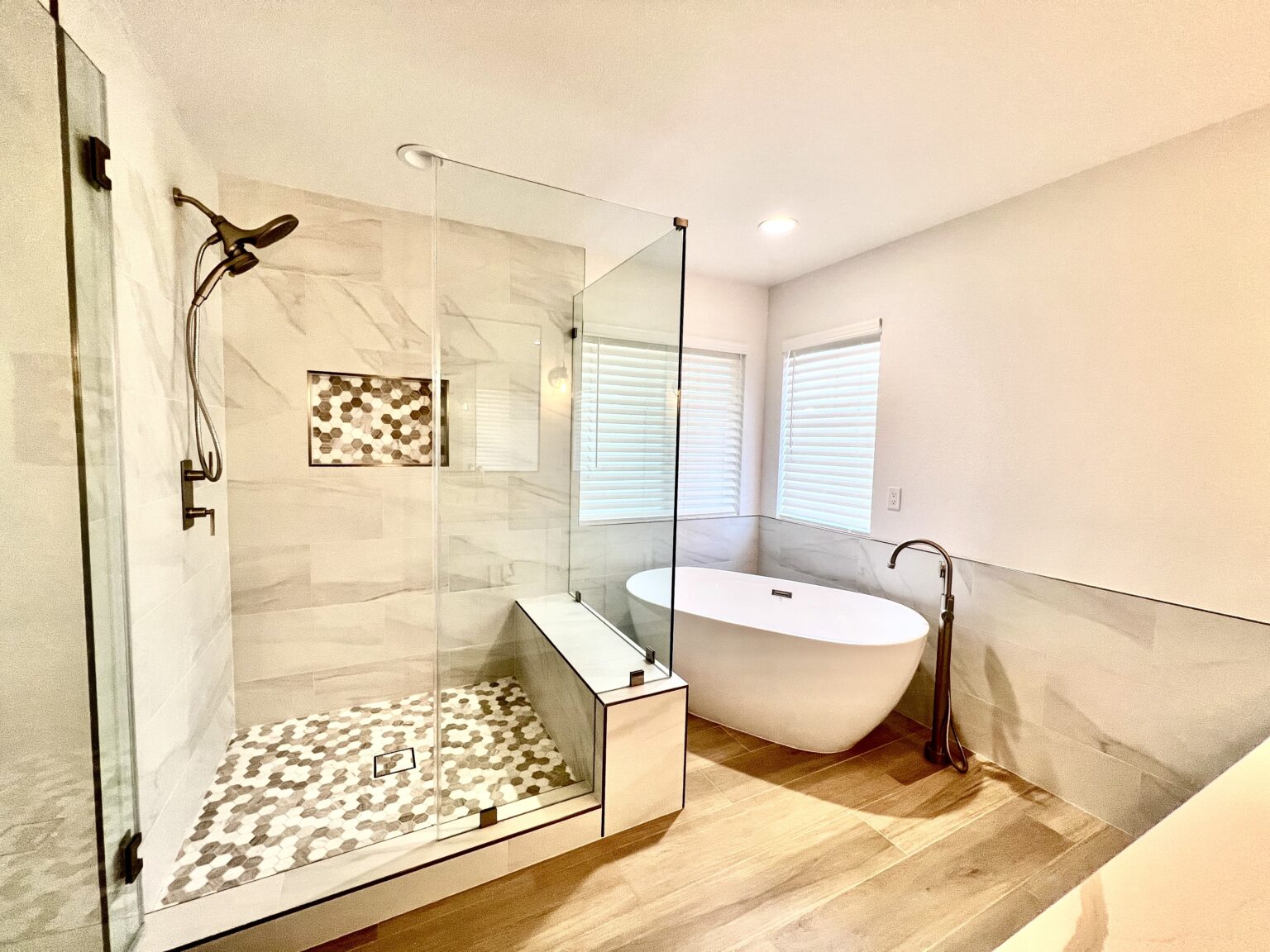 Walk in shower with a pebble tiled floor and brass fixtures, beside a freestanding tub.