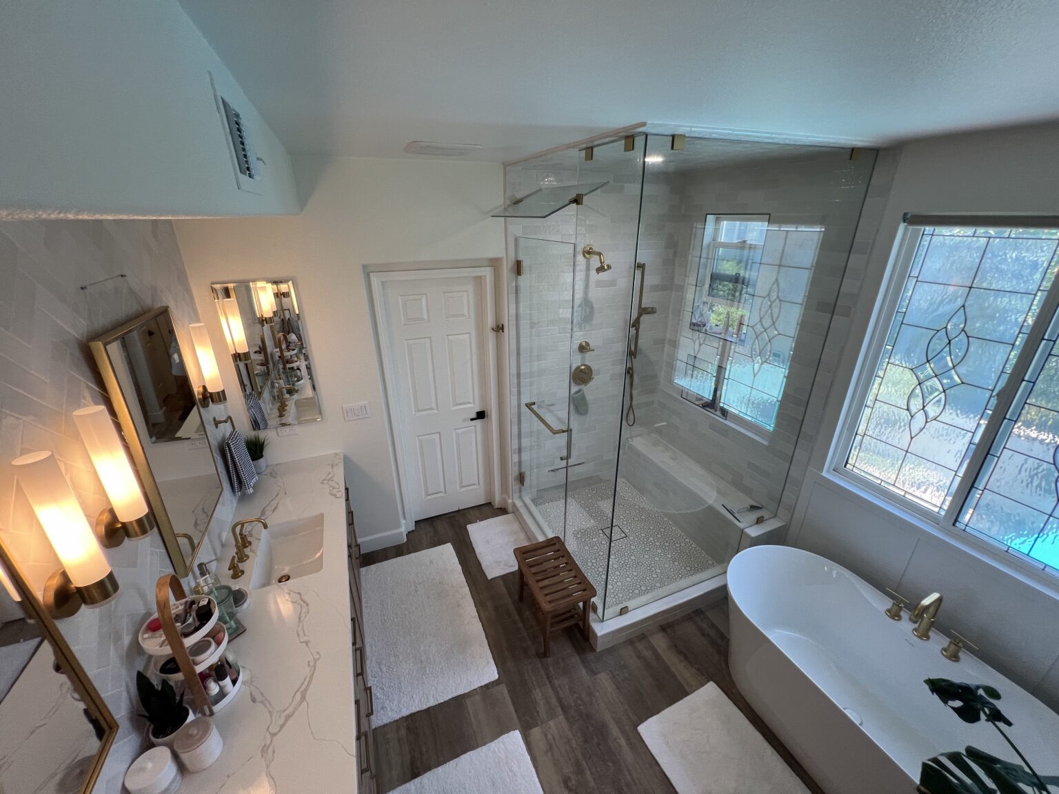 Bathroom with a glass shower, a freestanding tub and a wood floor, lit by a stained glass window.