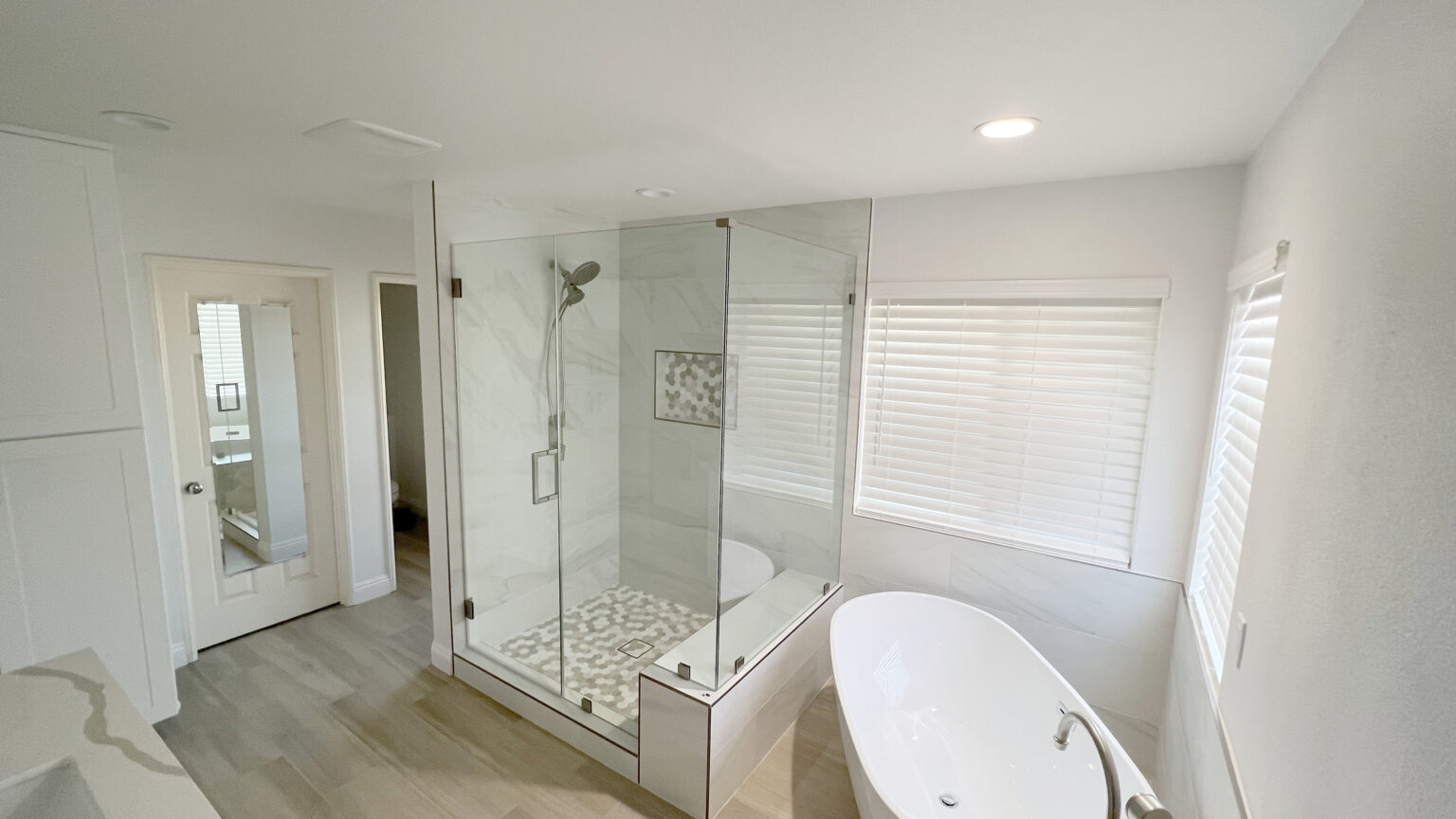 Bathroom with a wood look plank floor, a glass shower and a freestanding tub.