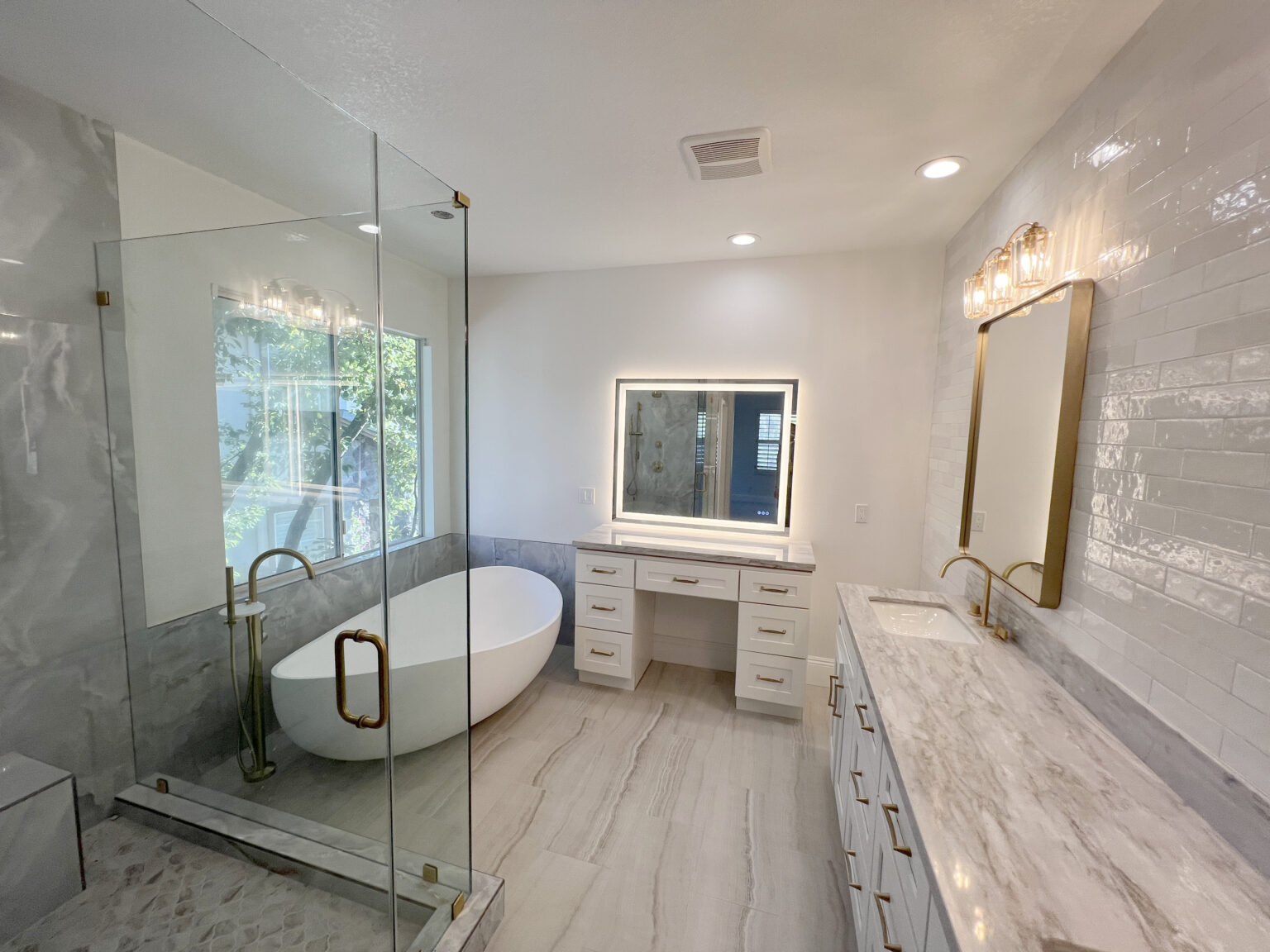 Bathroom with large format marble look wall tile, a freestanding tub and a makeup counter.