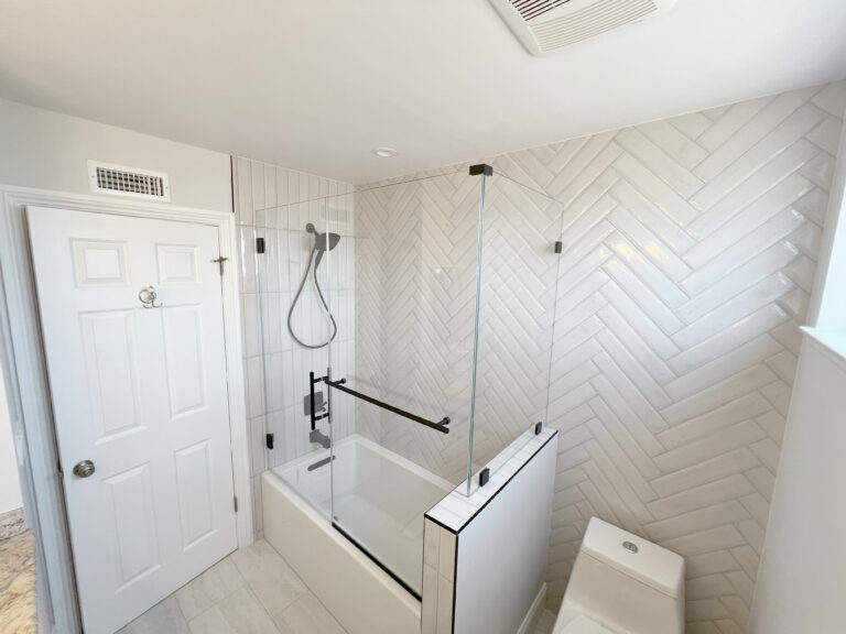 Bathtub with a glass screen and a shower over it, against herringbone tiled walls.