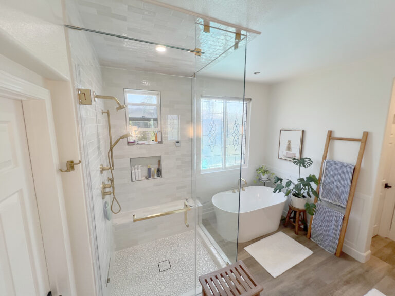 Walk in shower with a clear glass panel and brass fixtures, next to a freestanding tub.