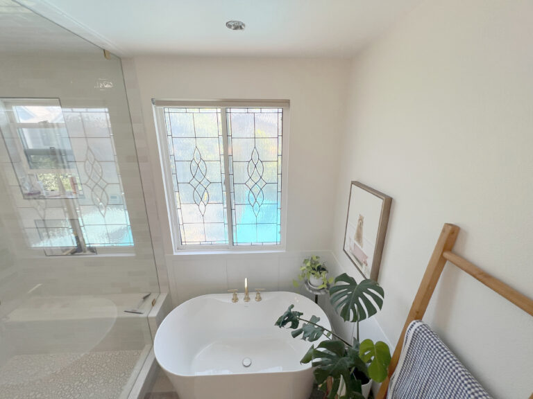 Bathroom with a freestanding tub under two windows and a glass shower beyond.