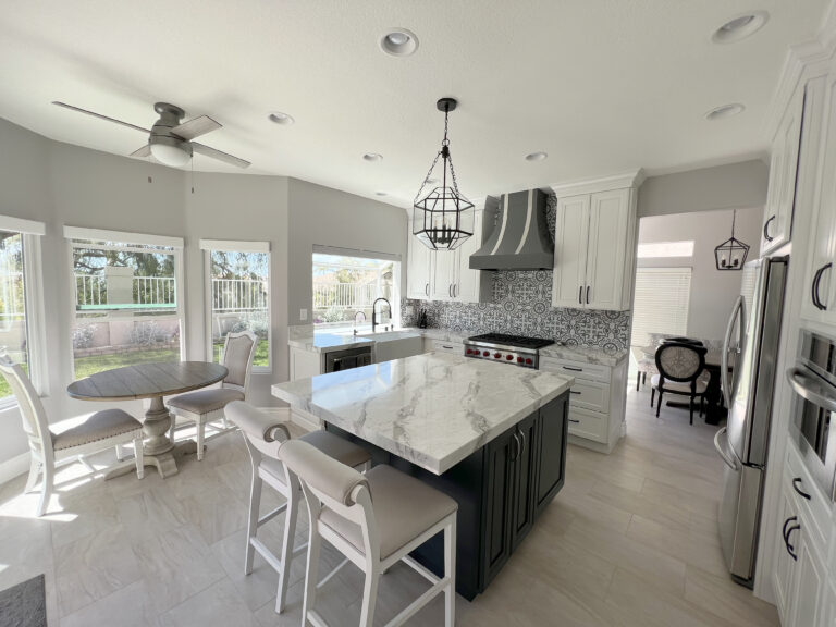 Open kitchen with a navy island topped in white stone with heavy grey veining, seating three.
