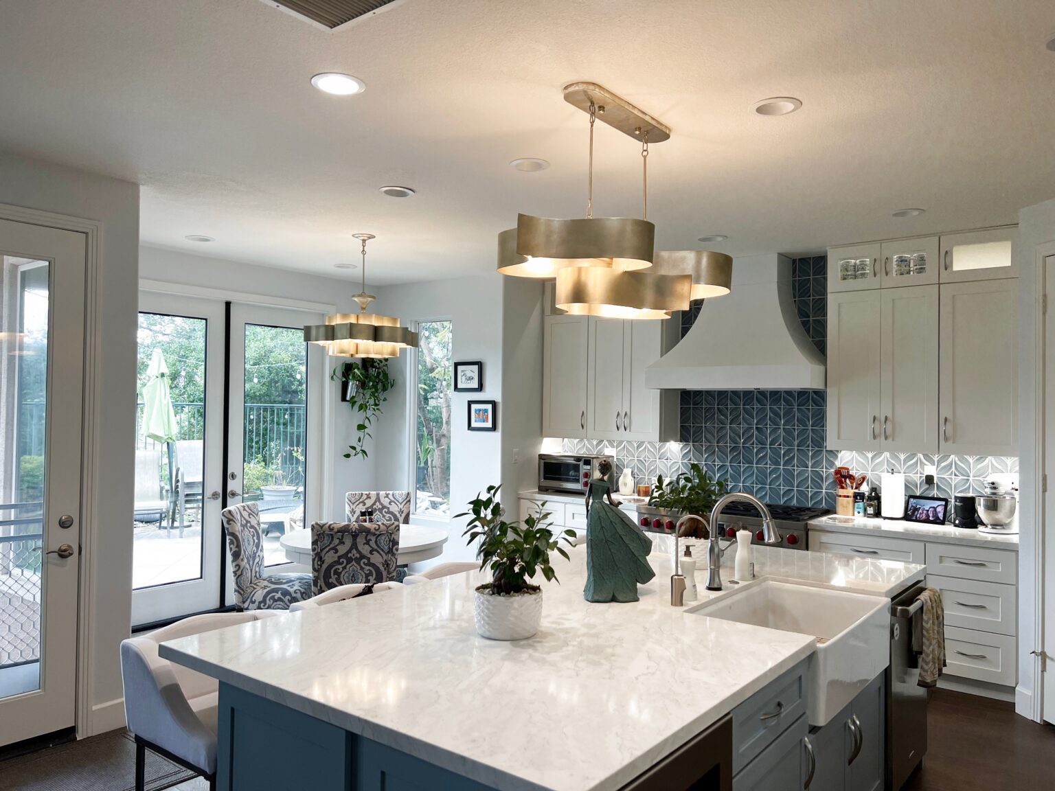 Kitchen with white shaker cabinetry, tall glass panelled upper cabinets and a navy blue island under two brass drum pendants.