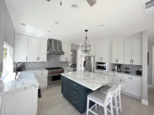 White shaker kitchen with a navy island, patterned tile backsplash, stainless range hood and lantern pendants