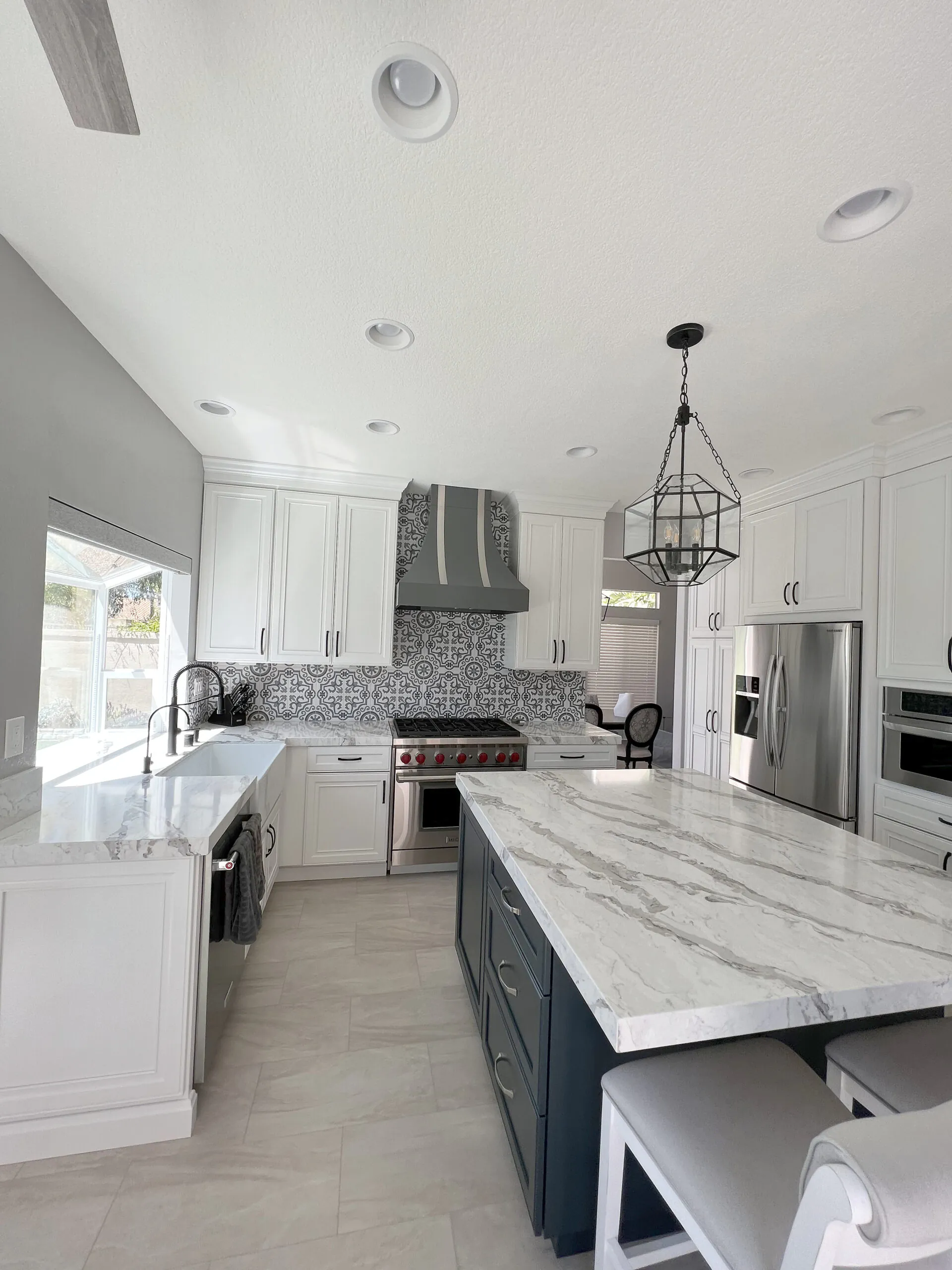 White kitchen with a navy island and marble counter seen from the dining side, with patterned tile backsplash