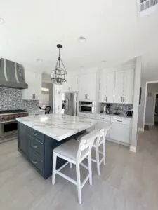 White kitchen with a navy island, patterned tile backsplash and a lantern pendant, seen from the entry