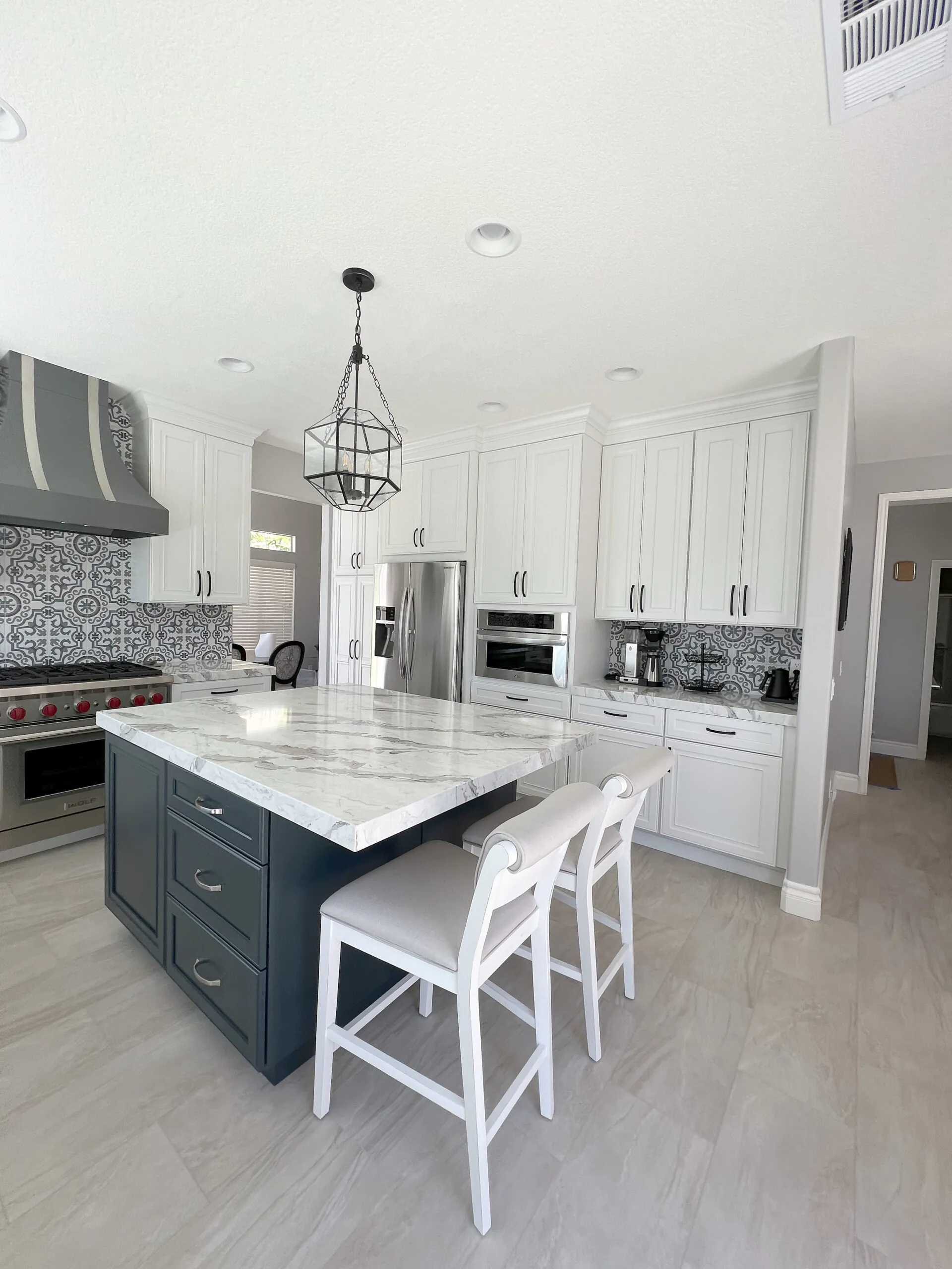 White kitchen with a navy island, patterned tile backsplash and a lantern pendant, seen from the entry