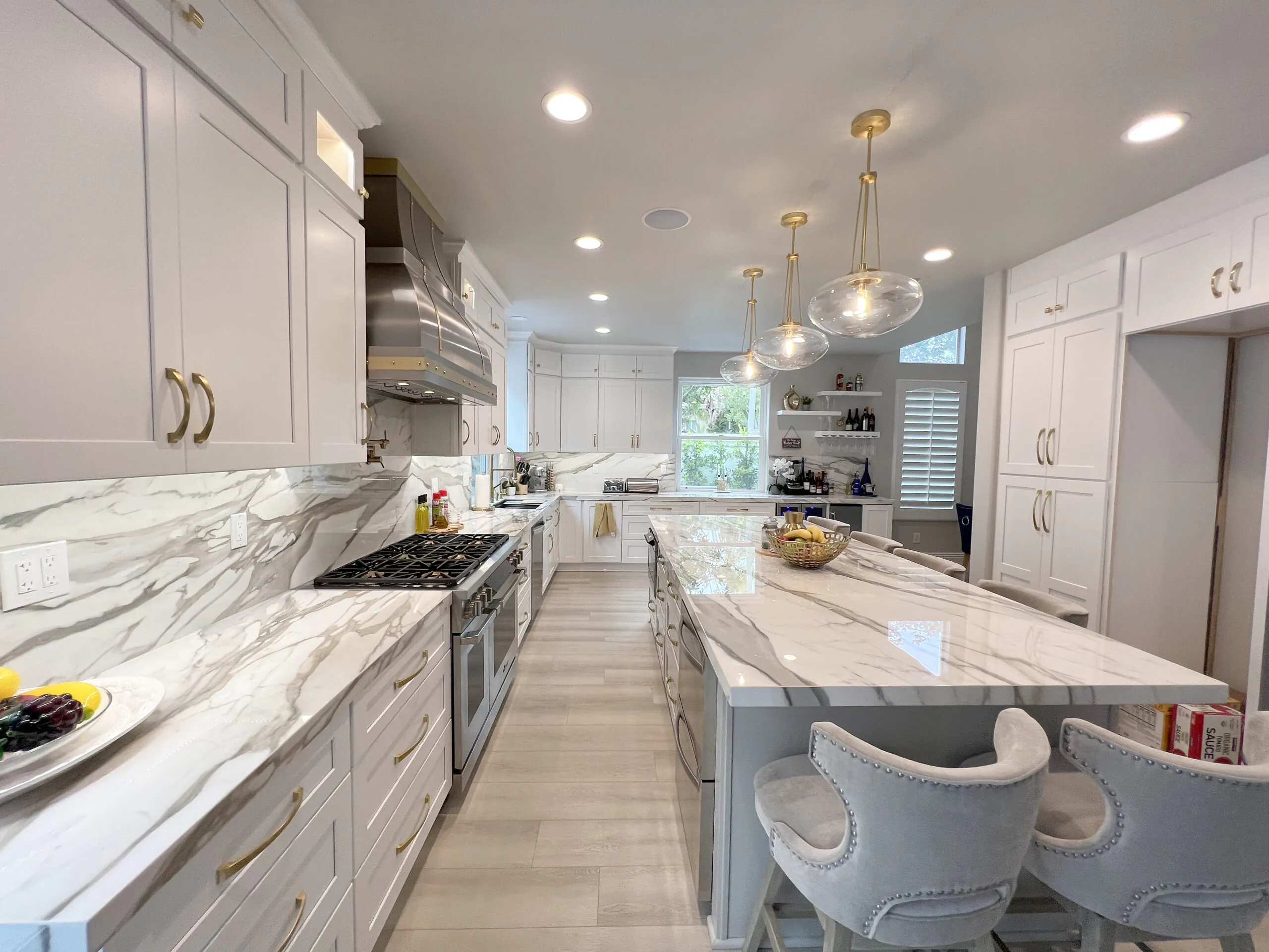 Kitchen with book matched marble backsplash and counters, brass pendants and upholstered island stools