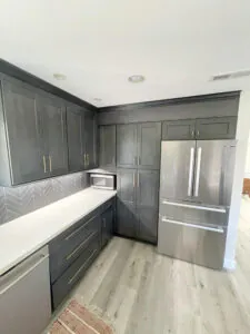 Charcoal grey cabinet run with white quartz counter, herringbone backsplash and panel ready refrigerator