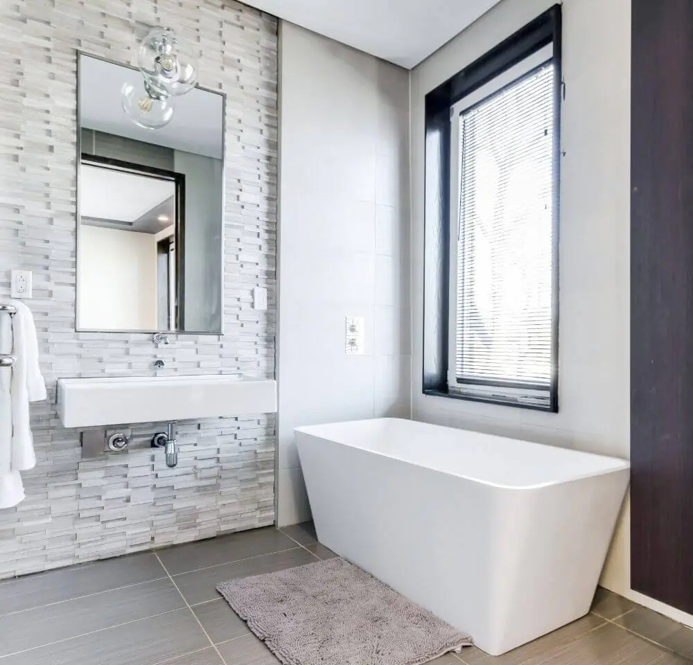 Bathroom with a stacked stone accent wall, wall hung basin and rectangular freestanding tub