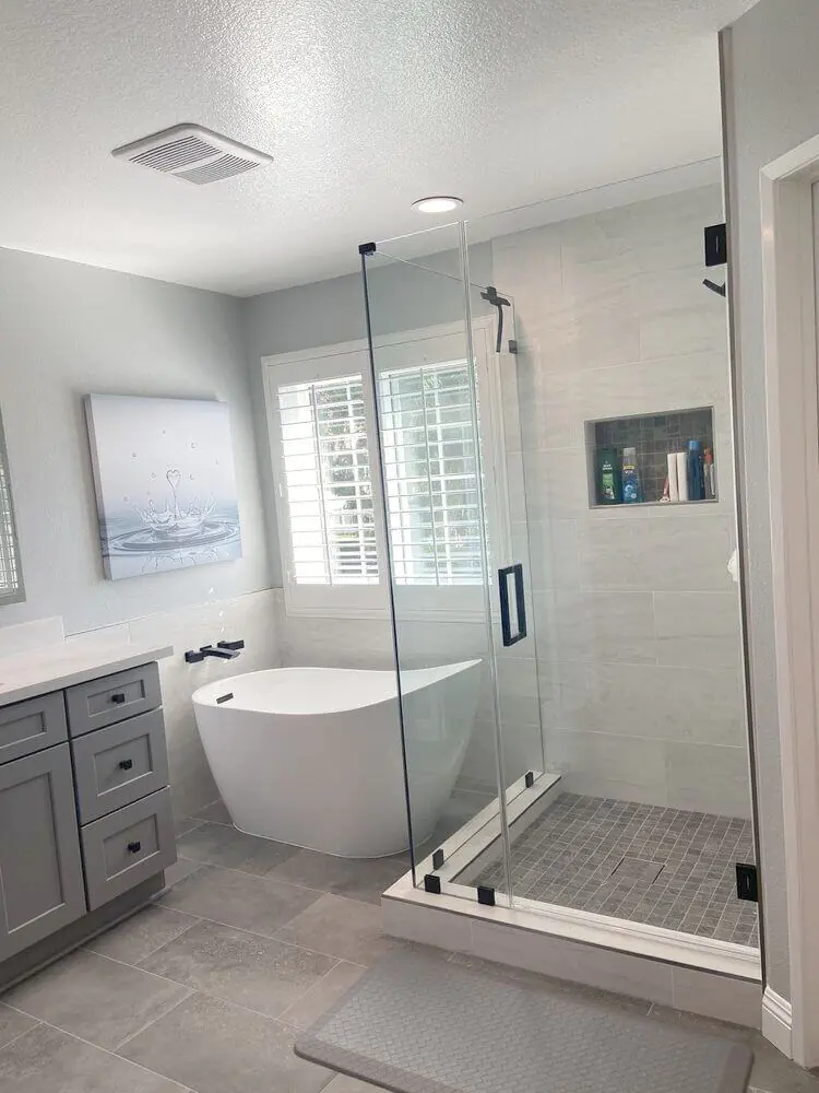 Bathroom with a grey vanity, freestanding tub and glass shower enclosure beside a shuttered window