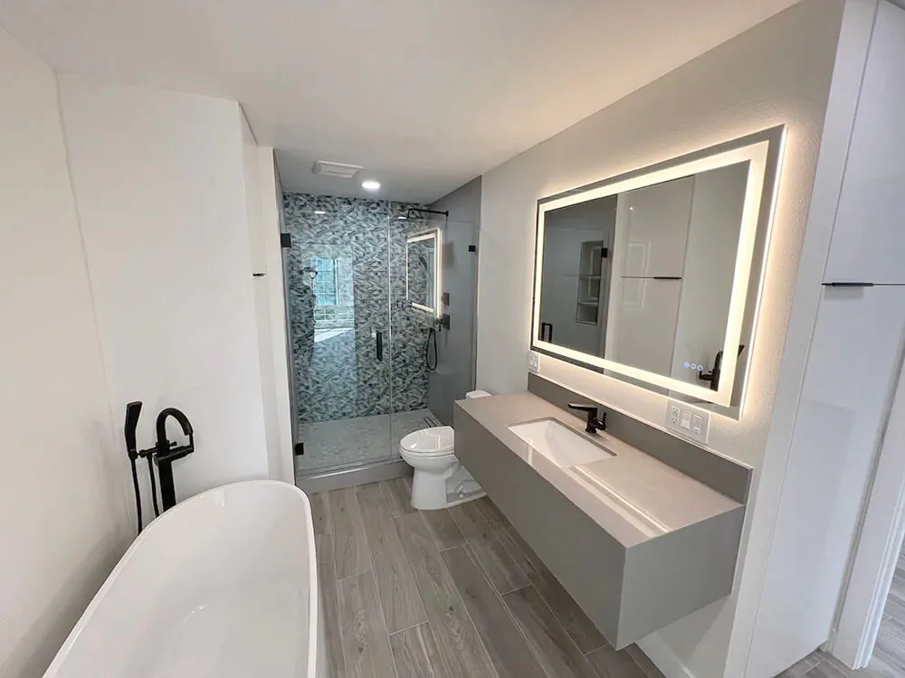 Bathroom with a backlit mirror, floating double vanity, freestanding tub and mosaic tiled shower