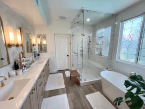 Wide master bathroom with double vanity, glass shower, freestanding tub and wood look flooring