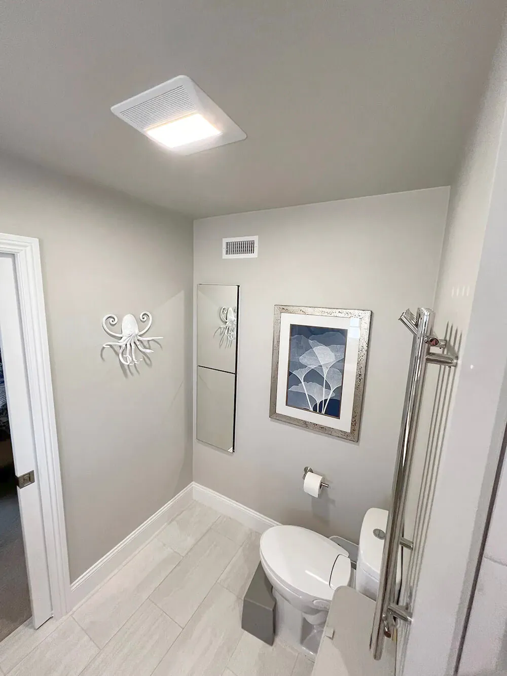 Compact bathroom with a wall mounted toilet, towel rail and framed print