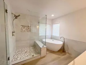 Marble tiled shower with a pebble floor and shelf niche, alongside a freestanding oval tub