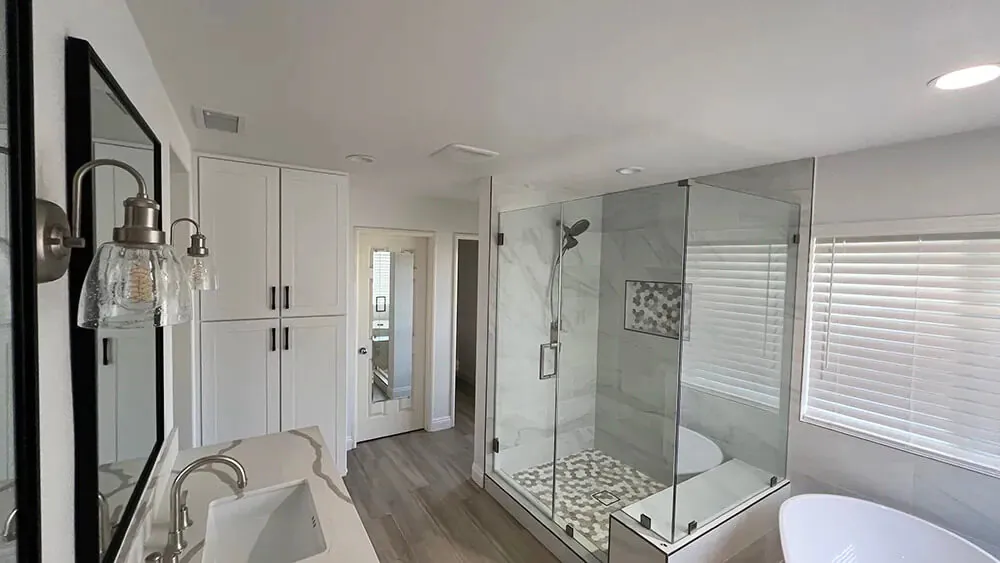 Bathroom with a black framed mirror, wall sconces and a glass shower with pebble flooring