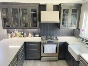 Two tone kitchen with navy lower cabinets, glass front uppers, herringbone backsplash and a farmhouse sink