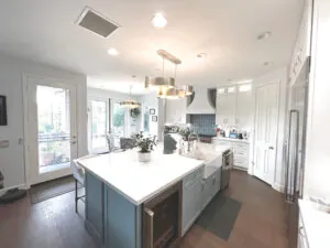 Wide kitchen with a grey island, white perimeter cabinets, a brass pendant and hardwood flooring