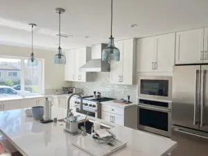 White kitchen with quartz counters, blue glass pendants, subway tile backsplash and stainless wall ovens