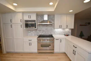 White shaker kitchen with a marble mosaic backsplash, professional gas range and stainless hood