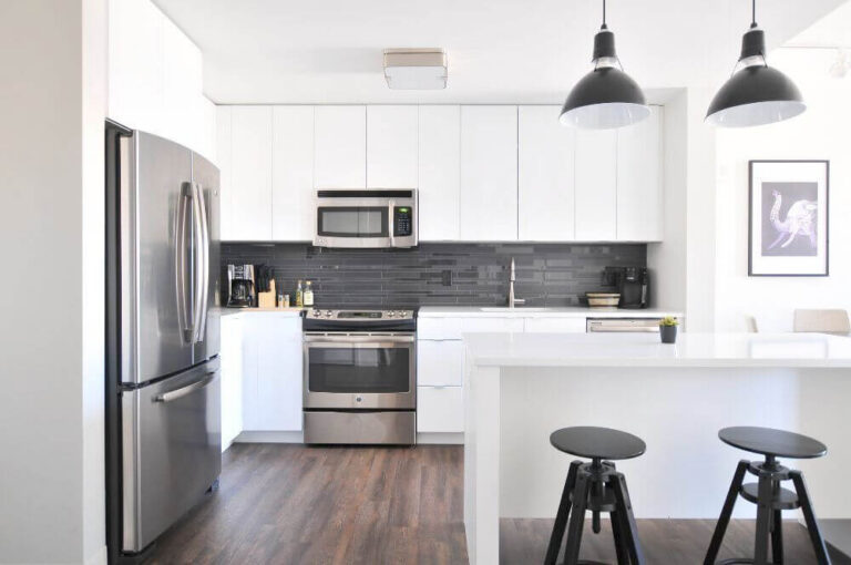 Kitchen with flat fronted white upper cabinets and no visible frame, above a dark tiled splashback.