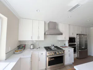 White kitchen with a stainless hood, gas range, subway tile backsplash and pale wood flooring