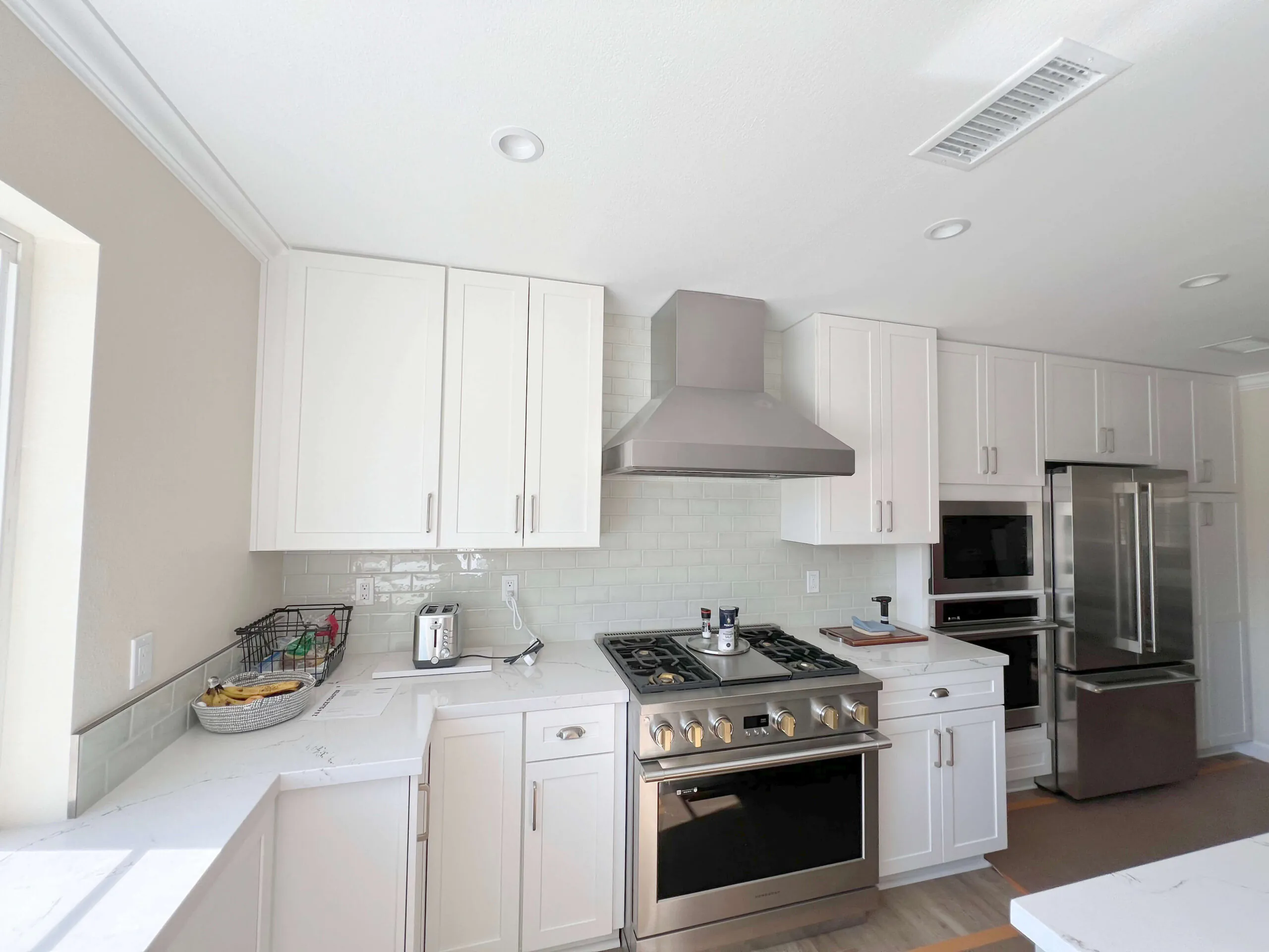 White kitchen with a stainless hood, gas range, subway tile backsplash and pale wood flooring