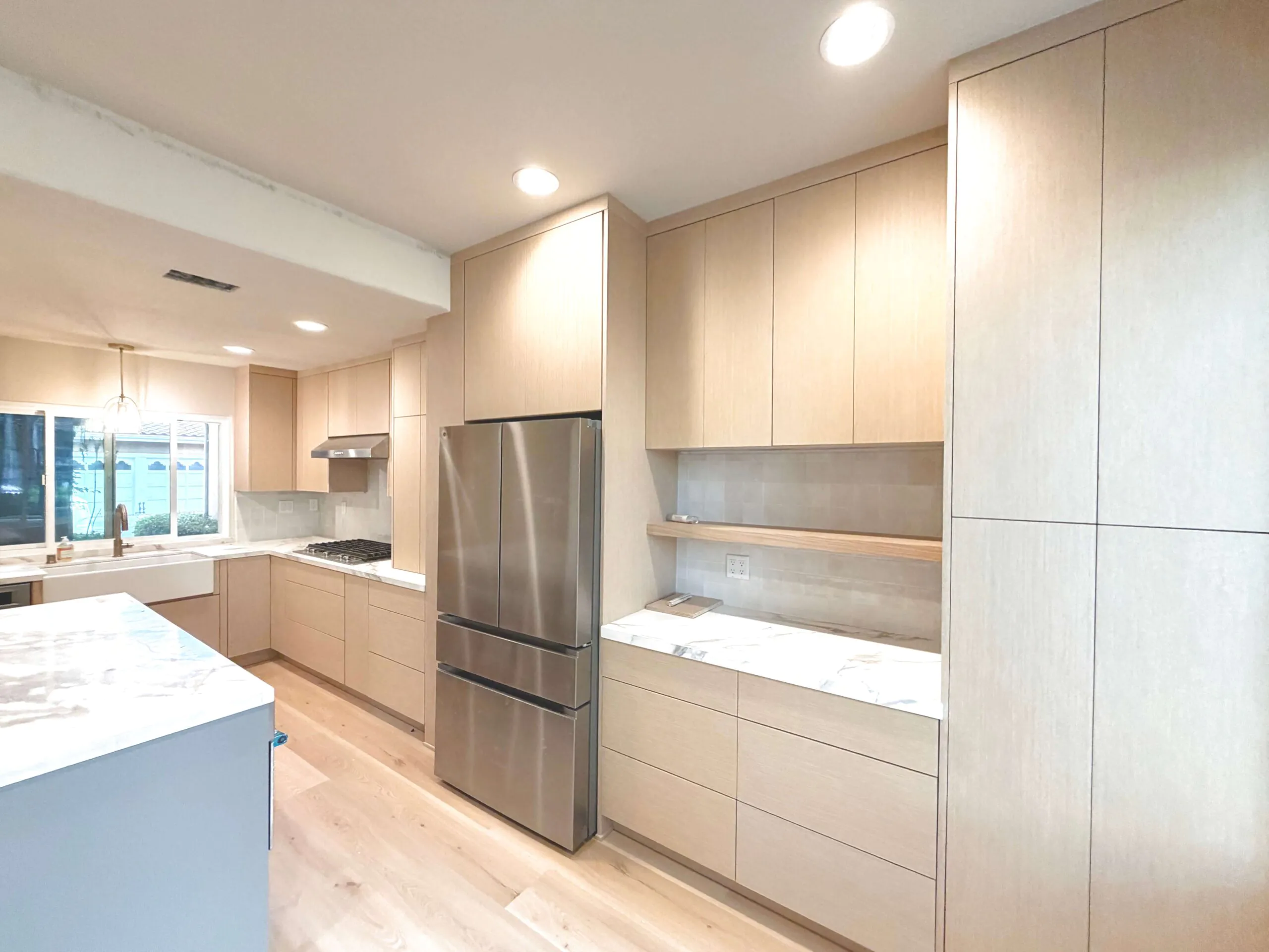 Pale oak flat panel kitchen with full height cabinetry, a marble island and a stainless refrigerator