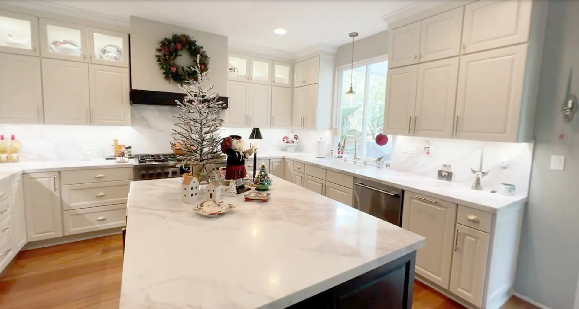 White kitchen with under cabinet lighting, a marble island and glass front upper cabinets